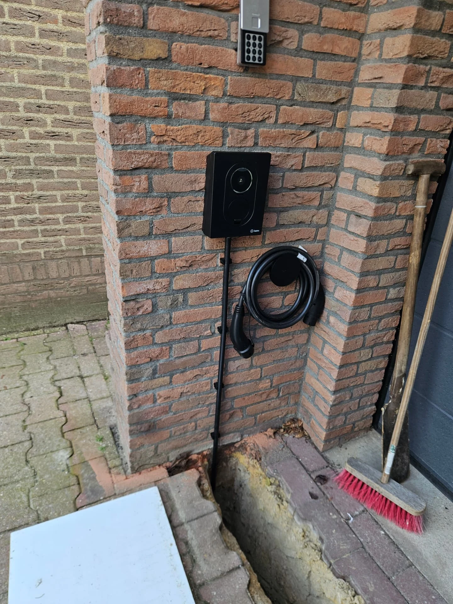 Zwarte Zaptec Go 2 laadpaal met laadkabel aan een bakstenen gevel in Klazienaveen