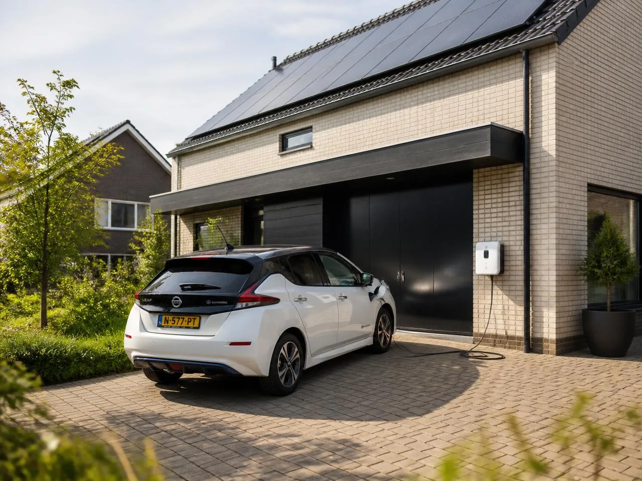Elektrische auto laadt thuis aan een laadpaal bij een moderne woning met zonnepanelen
